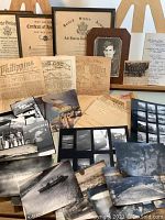 Overview of framed certificates, newspaper clippings, photographs, envelopes and negatives arranged on a table