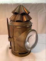 Antique brass candle lantern showing the vented top, convex glass lens, and brass body with patina.