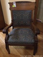 Front view of antique oak armchair showing upholstered seat and back, carved top rail and curved arms.