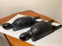 Two cast iron turtle figurines shown side by side on a wooden surface and white background, one black and one with green dots.