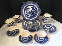 Photo of full set showing 7 dinner plates stacked, 10 tea cups with 3 saucers displayed, 1 fruit bowl to the side. Blue and white Blue Willow pattern visible.