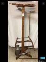 Full view of Swedish wooden rack with four arms, standing tall, showing attached pegs and grouped items below including milk can, hand rake, syrup siphon, and buck saw.
