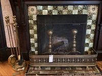 Brass fireplace screen, bumper, and pair of brass andirons positioned in front of tiled fireplace