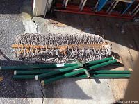 Hammock rolled up showing rope netting and wooden spreader bars alongside disassembled green metal stand parts.