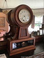 Full view of the wooden mantel clock on a furniture surface, showing circular clock face with glass and wooden body.