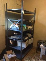 Metal storage shelving unit in a room with pegboard wall. Shelves currently holding boxes and miscellaneous items that are not included in the sale.
