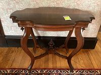Full side view of the wooden side table showing chimera style top and curved legs with brass casters.