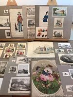 Photo showing a variety of Victorian era prints and cuttings mounted on grey paper including images of people in period dress, natural history scenes, and landscapes.