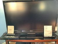 Front view of TV and Blu-ray player on stand with manuals and remotes