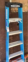 Werner 6-foot step ladder with blue fiberglass rails and aluminum steps, label showing load capacity and other specifications.