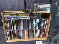 Photo of over 100 CDs stacked in a cardboard box and on top, showing a variety of artists and genres