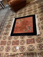 Photo showing large kilim rug with geometric brown tone patterns and smaller floral motif rug on top