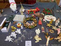 Overview of the lot on a dark surface, showing varied angel ornaments, wreaths, small figurines, and Christmas decor including a red rocking horse and Merry Christmas plaque.