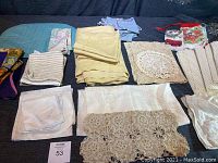 Full view of assorted folded table linens including crocheted runners and doilies, aprons, and towels.