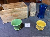 Photo showing the old wooden Canada Dry crate with worn markings, two McCoy flower pots in green and yellow with matching saucers, and tall pottery piece.