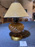 Front view of antique lamp showing swirled gold-colored glass body, brass base, beige woven fabric lampshade, and electric cord.