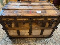Front view of antique wood trunk with metal reinforcements, latches and handles. Trunk shows wear and patina consistent with age.