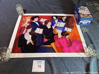 Overview of first art print with seven people holding books, set under glass weights for display
