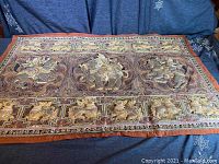 Full view of a large embroidered rectangular tapestry featuring animal motifs and intricate border designs on a dark background