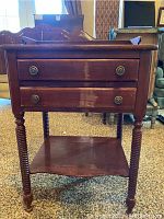 Front view of cherry side table showing two drawers with brass-colored knobs and turned legs.