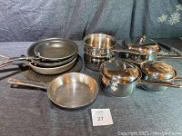 Cookware set displayed showing stacked frying pans next to pots and lids on a dark cloth background.
