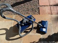 Blue Kenmore canister vacuum with hose and wand shown on tiled and concrete floor surface.