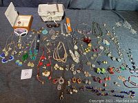 Overview of large assortment of costume jewelry including necklaces, earrings, bracelets, rings, brooches, watches, sunglasses, a jewelry box, and a wire basket.