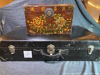 Large black retro suitcase and painted oriental wooden chest displayed together.