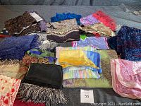 Photo showing a variety of scarves in different patterns and colors spread on a surface along with a pair of black leather gloves.