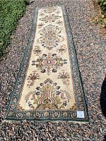 Full length view of the wool oriental runner on gravel showing the entire rug's pattern and condition.