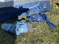 Blue and white Sierra Designs branded tent fabric and poles laid on green grass surface with stakes and ground cover.