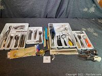 Full lot showing trays with silverware, wood utensils, kitchen tools and various wine openers on a dark cloth.