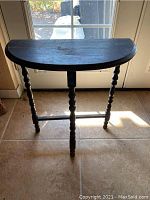 Small half-moon shaped wooden side table in dark finish shown from front with visible turned legs.