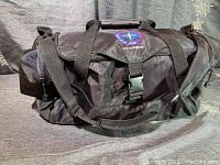 Ogio 55L black duffel bag with adjustable straps and central buckle shown fully zipped, soft sided.