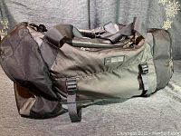 Black and gray REI mega duffle 65L showing side with straps and logo patch