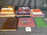 Wide view of the collection showing a large assortment of hardcover and paperback books, including prominently a dark brown leather-bound book titled 'Leaves of Gold', a pink architecture book titled 'Lodge of the Imagination', plus many colorful cookbooks.