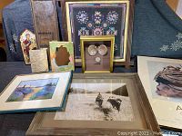 Wide view showing multiple framed artwork items including embroidery, pearls, photos, and posters.