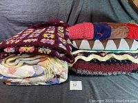 Photo showing seven folded blankets: colorful granny square crochet afghan, pastel patterned quilt, striped wool blanket, zigzag crocheted afghan, and others stacked.