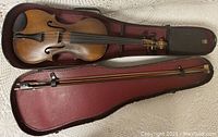 Violin and bow inside the open burgundy-lined case showing the full instrument and bow length.
