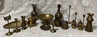 Overview image showing the assorted brass items including candle holders, vases, bowls, and small containers arranged on lace fabric.