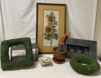 Photo showing assorted items including framed sunflower art, moss-covered frames, pot with tools, terrarium, and book.