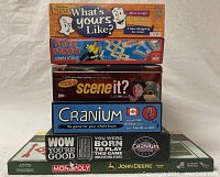 Front view of the stack of six board games including What's Yours Like?, Stick Storm Cobra Strike, Seinfeld Scene It, Cranium, and John Deere Monopoly