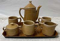 Photo showing full tea set with teapot, three teacups, sugar bowl, creamer, all on brown plastic serving tray.