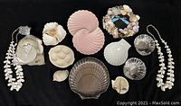 Overhead view of all items in the collection arranged on a black background, showing a variety of sea shell-shaped plates, shell art, shell garlands, and bowls.