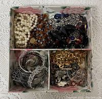 Top view of floral organizer filled with costume jewelry showing pearls, silver and gold chains, and earrings.