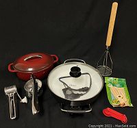 Full lot photo showing KitchenAid cast iron pot, Oster electric skillet, 48-pack bamboo skewers, plastic measuring spoons, metal potato ricer, metal cheese grater, and large potato masher.