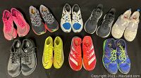Top-view photo of all 9 pairs of athletic shoes arranged in two rows on a carpeted floor in various colors including pink, gray, blue, neon yellow, red, black, and beige.