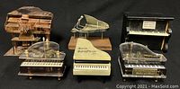 Five small piano figurines and music boxes arranged front and center against black background, sizes about 3 to 4.5 inches tall, including onyx piano and several black music boxes.