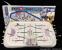 Photo of the hockey game rink with attached rods and hockey player figures in plastic bag, shown alongside the original box with hockey-themed graphics.