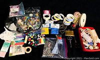 Wide view of sewing supplies showing scissors, many spools and bobbins of thread, ribbons, lace, and pin cushions organized on a black surface